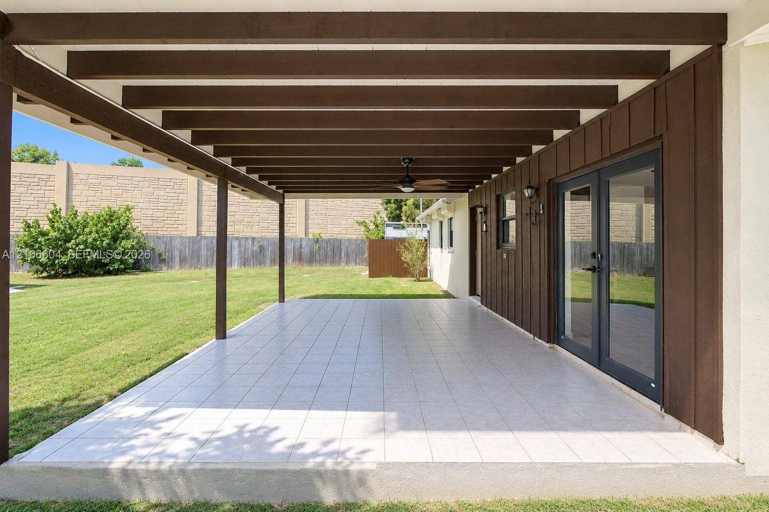 Covered patio featuring exposed wooden ceiling beams, tiled flooring, an integrated ceiling fan, and double glass doors with dark framing