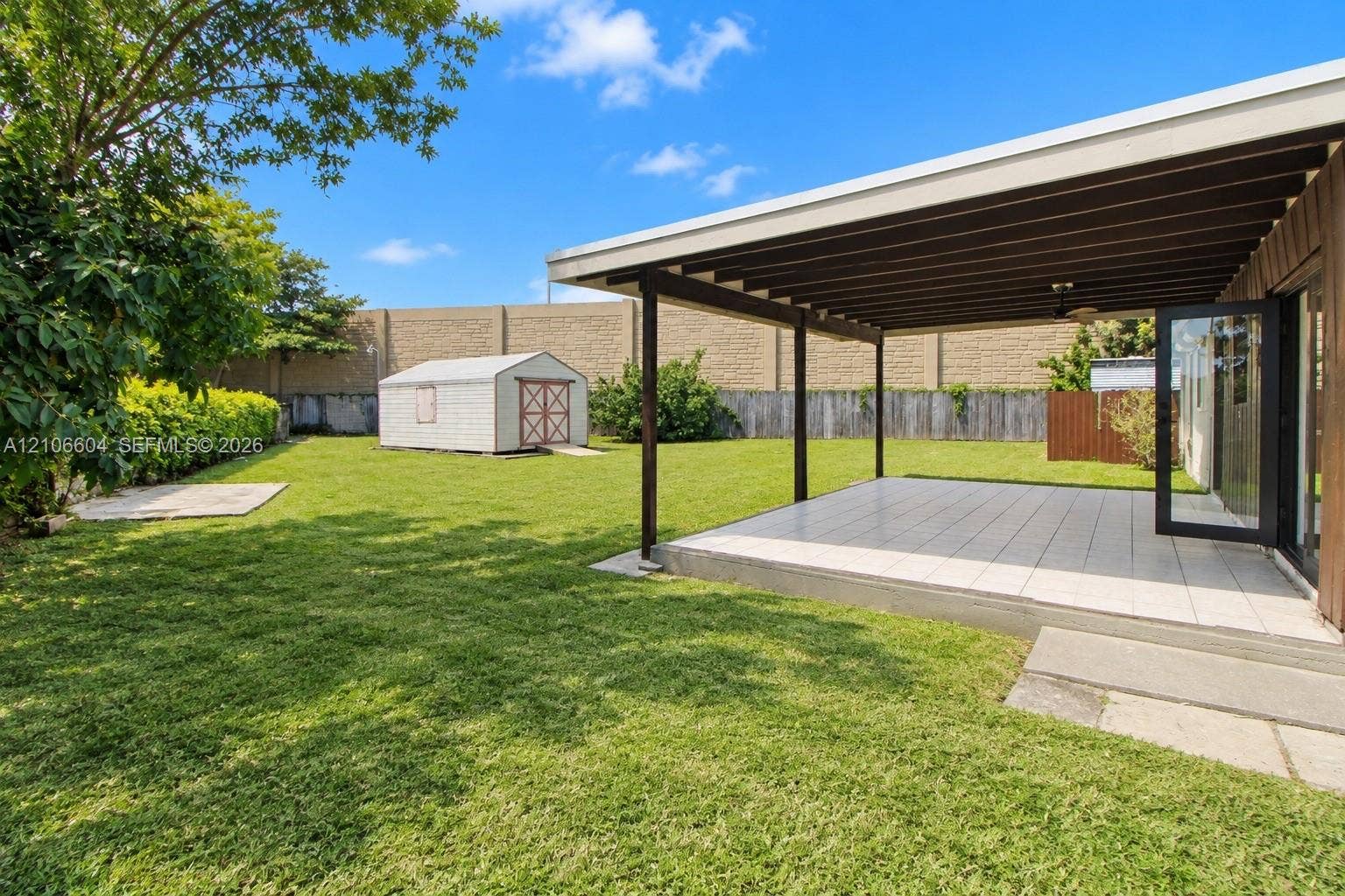 Backyard featuring a covered patio with tile flooring, an expansive lawn, a standalone storage shed, and masonry perimeter wall