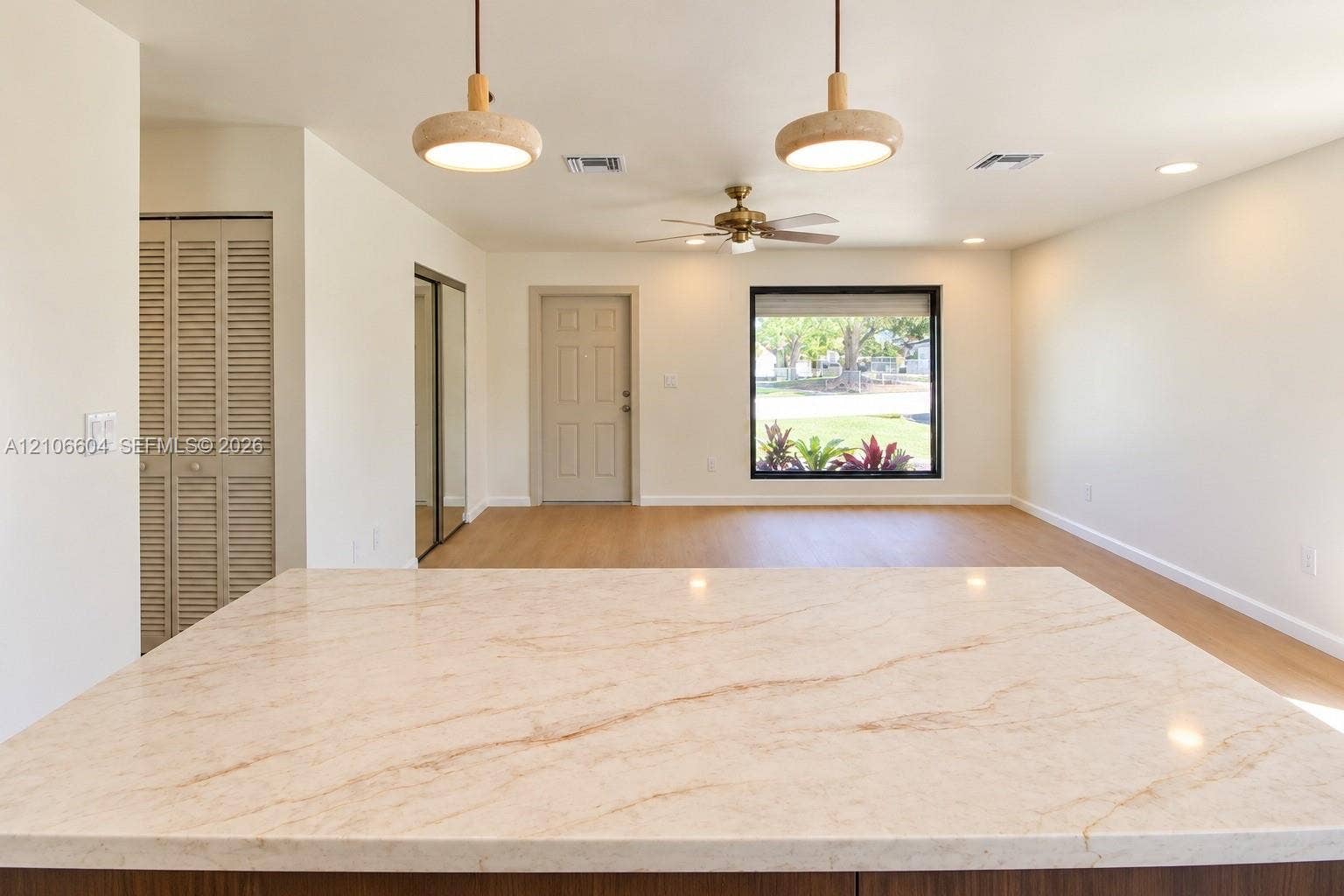 Solid-surface countertop with neutral veining, wood-finish flooring, dual pendant lighting, ceiling fan, and louvered closet doors