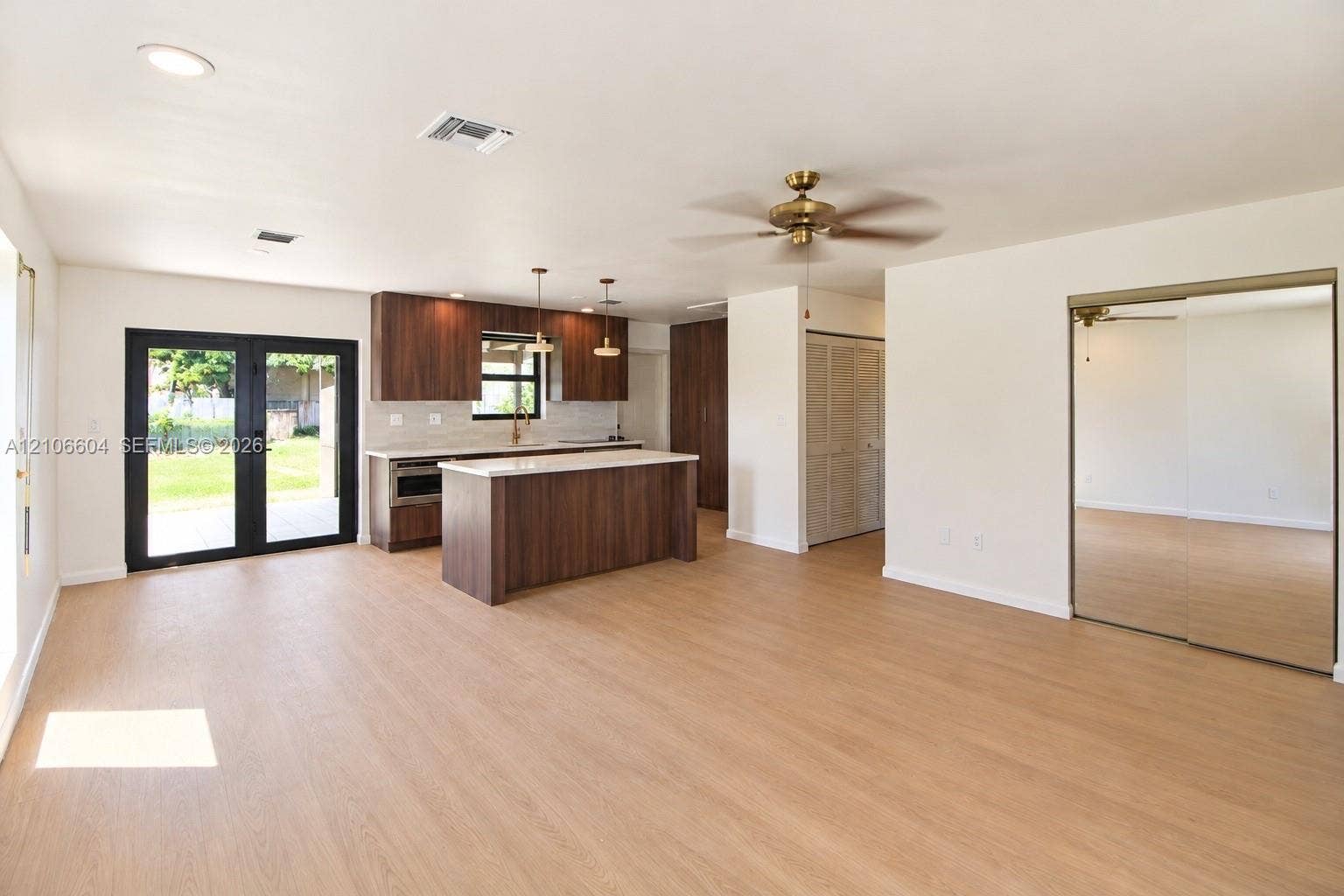 Open-concept kitchen featuring dark wood-finish cabinetry, a center island with a stone-composite countertop, light wood-finish flooring, dual French doors with black frames, and floor-to-ceiling mirrored closet doors