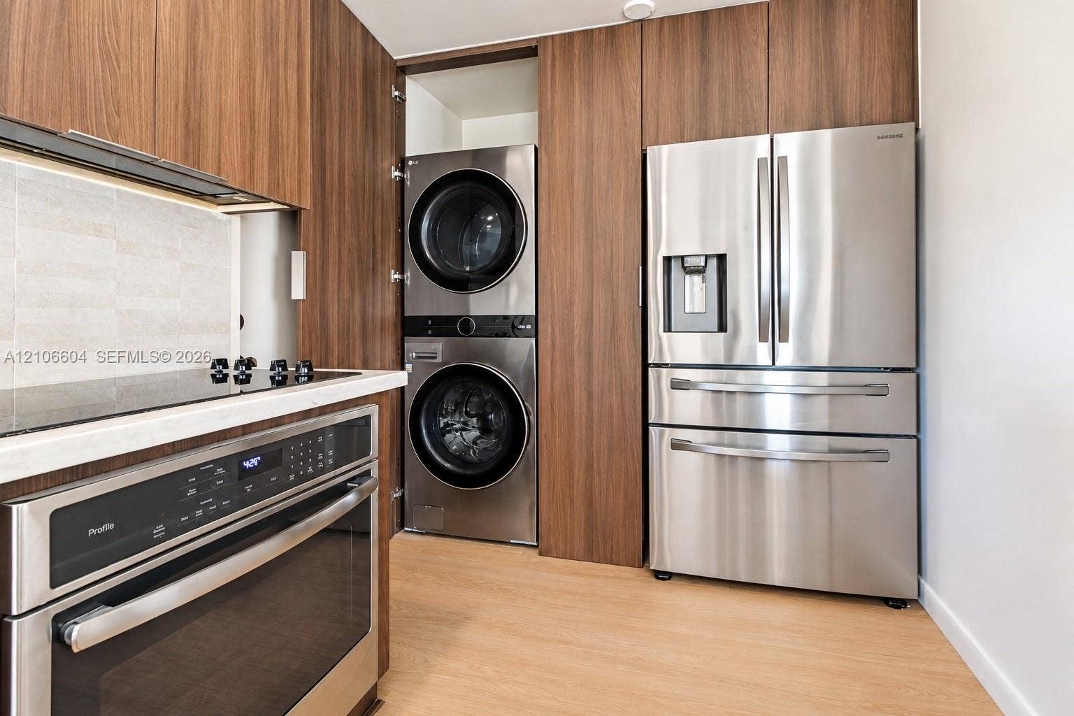 Custom wood-finish cabinetry, stainless steel appliances, integrated laundry, smooth-finish countertop, and wood-finish flooring