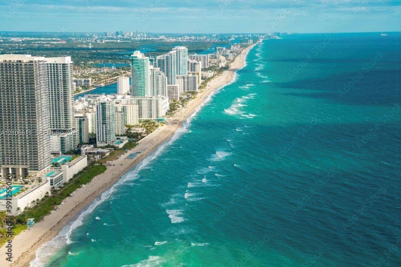 17570 Atlantic Boulevard, #105, Sunny Isles Beach, Sunny Isles Beach, FL 33160 Multi-story exterior featuring white stucco siding, metal-roofed covered parking, and palm trees