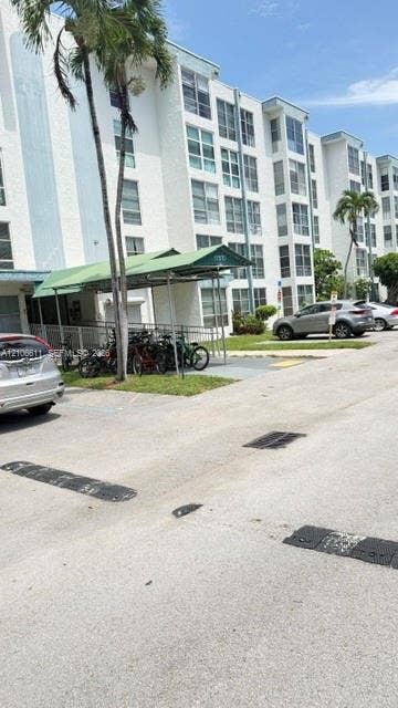 17570 Atlantic Boulevard, #105, Sunny Isles Beach, Sunny Isles Beach, FL 33160 Multi-story exterior featuring white stucco siding, metal-roofed covered parking, and palm trees