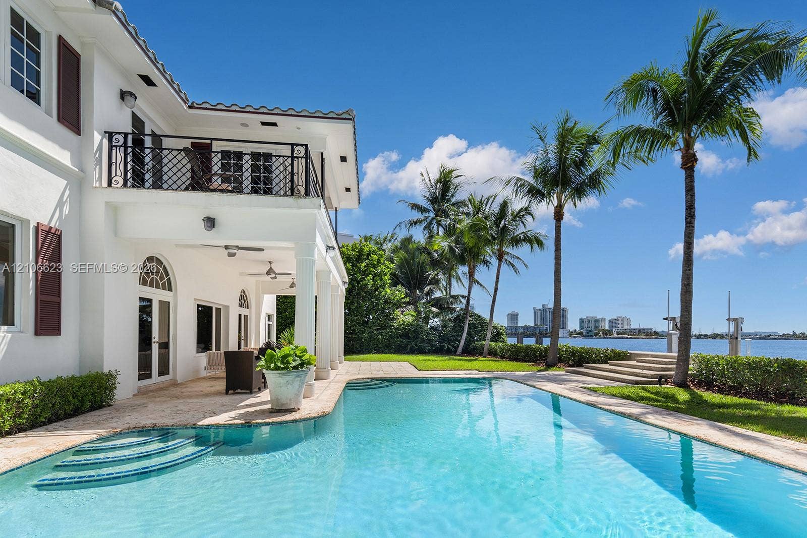 2312 Bay Avenue, Miami Beach, FL 33140 Waterfront residence featuring a private swimming pool, expansive stone patio, elevated balcony with ornate metal railing, and direct water access