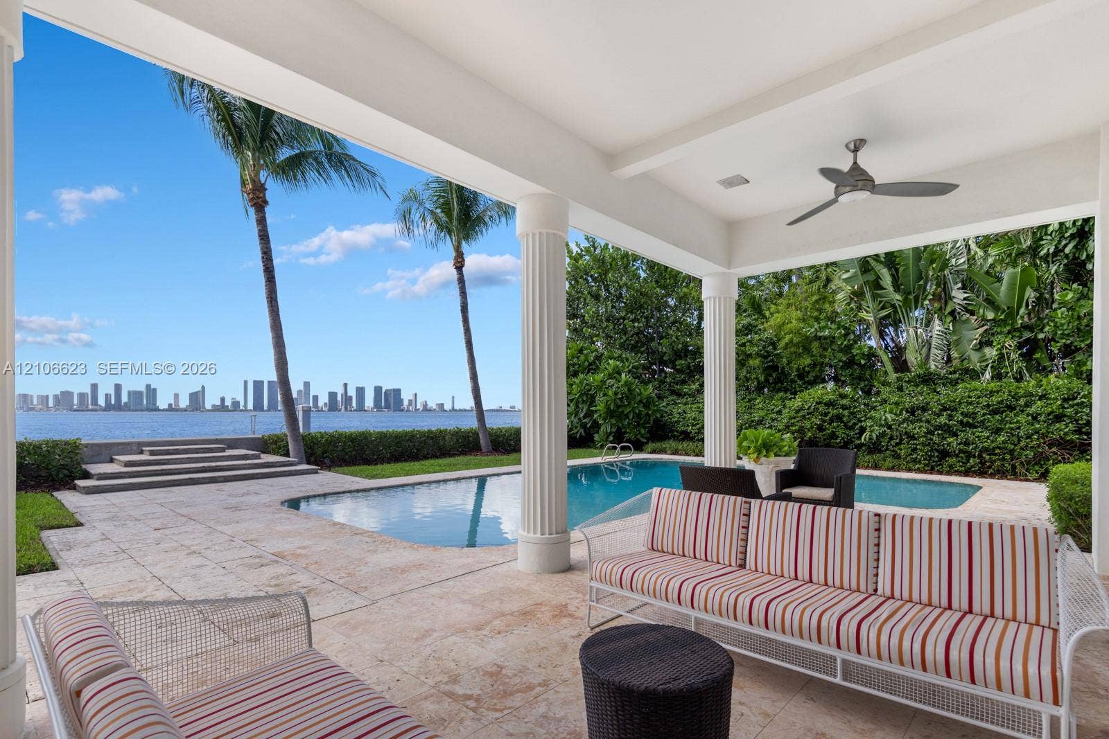 2312 Bay Avenue, Miami Beach, FL 33140 Covered patio featuring stone tile flooring, structural columns, and a ceiling-mounted fan, overlooking an in-ground swimming pool and waterfront with skyline backdrop