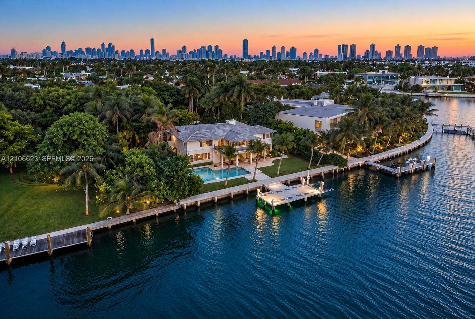 2312 Bay Avenue, Miami Beach, FL 33140 Waterfront property featuring a private dock, swimming pool, manicured lawn, and mature landscaping with a city skyline backdrop