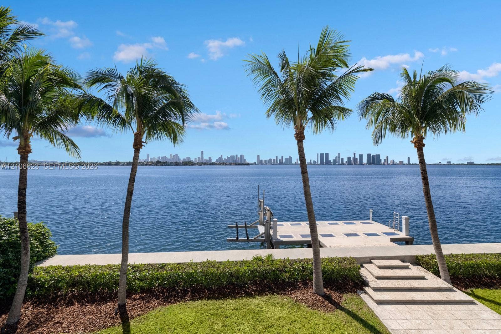 2312 Bay Avenue, Miami Beach, FL 33140 Waterfront property featuring a private dock, stone-paved walkway, manicured hedging, and mature palm trees