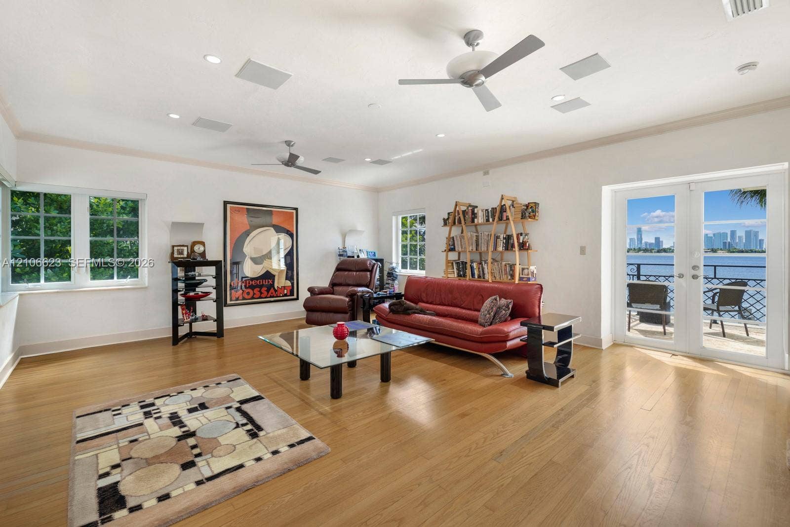 2312 Bay Avenue, Miami Beach, FL 33140 Spacious room featuring wood-finish flooring, multi-pane windows, dual ceiling fans, recessed lighting, and double-glass doors opening to a balcony with waterfront and skyline scenery