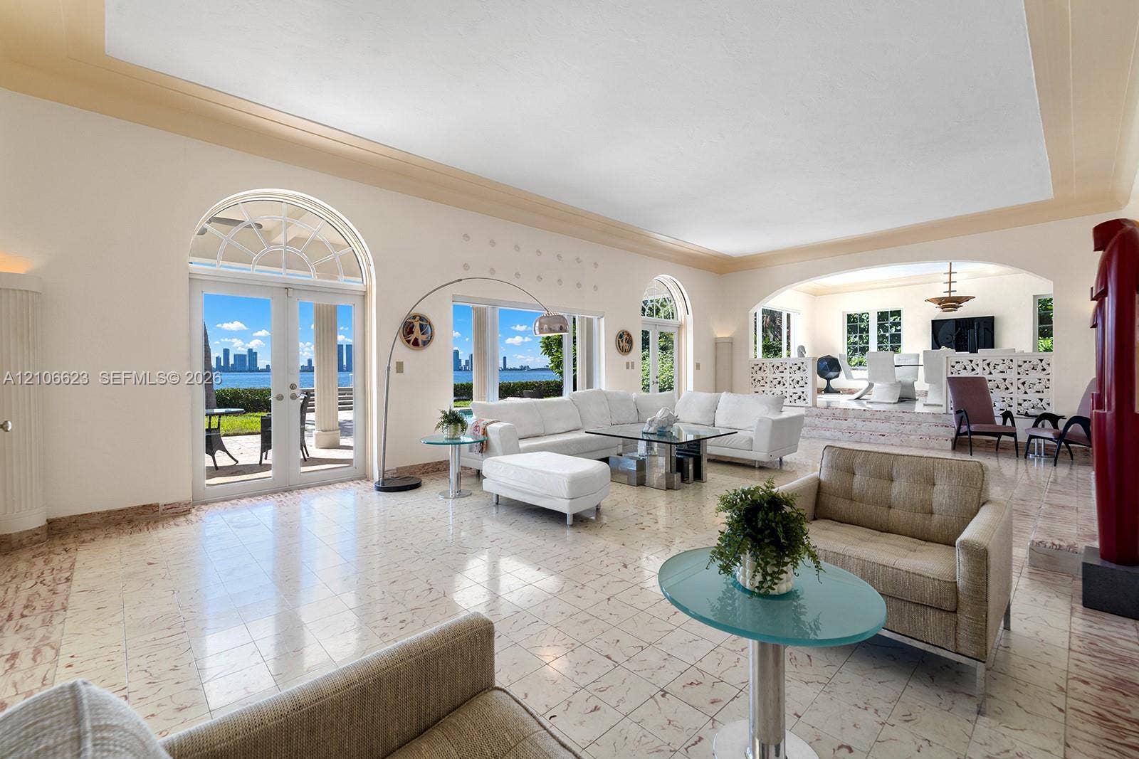 2312 Bay Avenue, Miami Beach, FL 33140 Open-concept interior featuring light-toned stone flooring, arched glass double doors, elevated platform area with decorative latticework, and recessed tray ceiling detailing