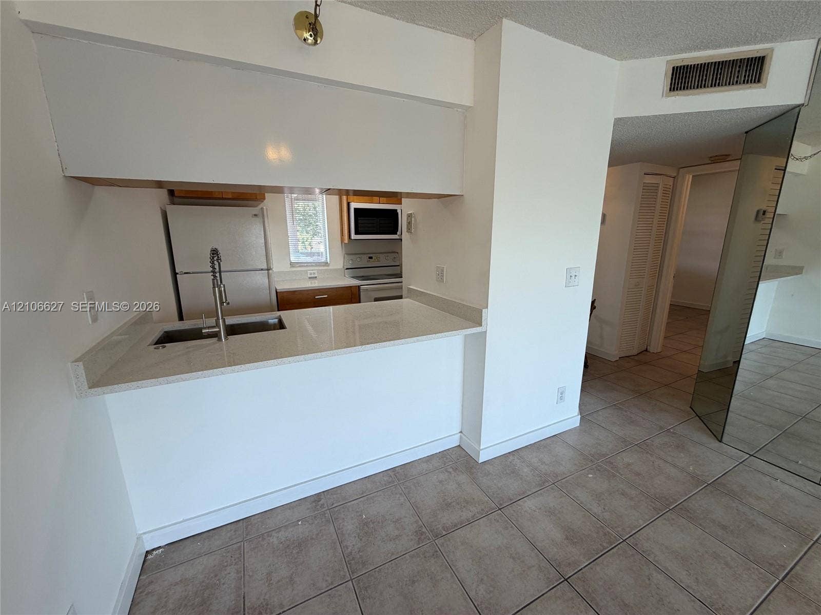 Kitchen featuring a peninsula with a composite countertop, an undermount stainless steel sink, a gooseneck faucet, tile flooring, and mirrored paneling