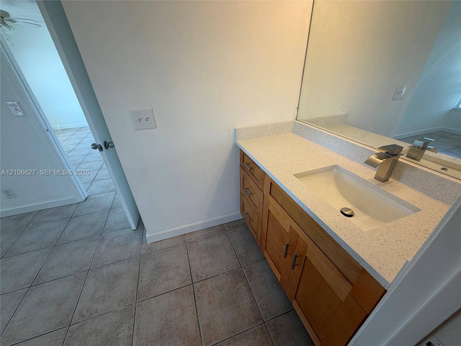 Vanity featuring light wood-finish cabinetry, a light-toned solid surface countertop, an integrated rectangular sink, a single-handle metal faucet, and a large-format mirror