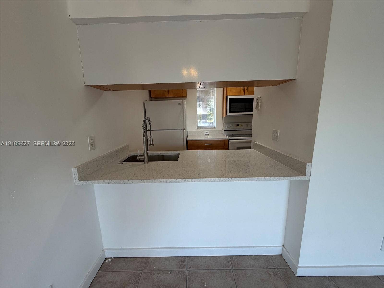 Pass-through kitchen featuring a solid-surface countertop, undermount sink with a gooseneck faucet, upper cabinetry, and integrated kitchen appliances