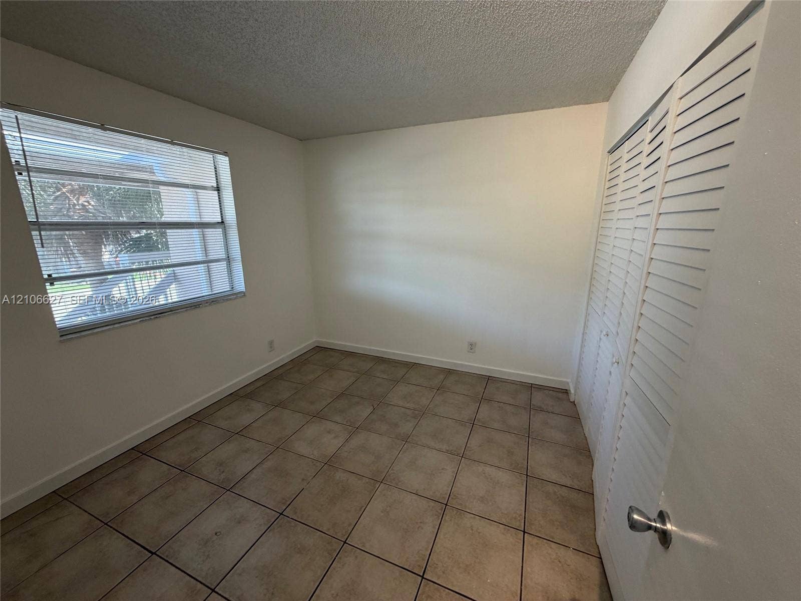 Neutral-toned tile flooring, louvered bi-fold closet doors, and horizontal slatted window blinds