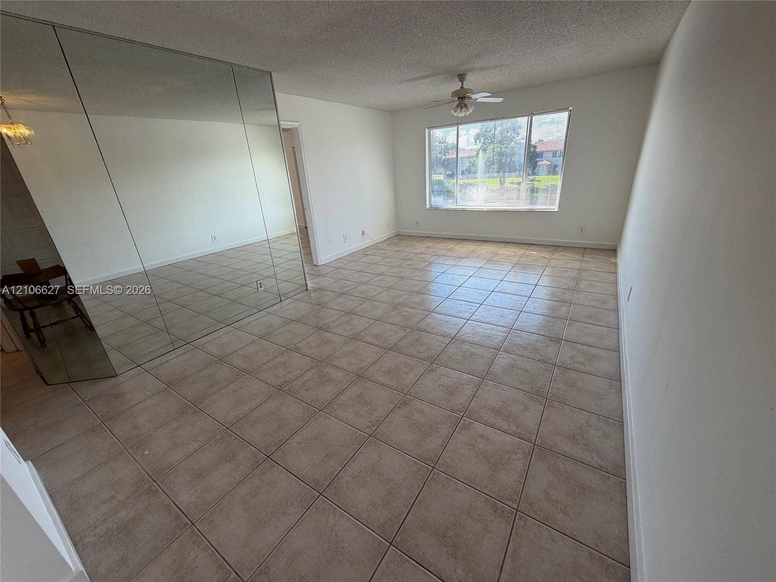 Spacious room featuring floor-to-ceiling mirrored wall paneling, tile flooring, large multi-pane window, and a ceiling fan