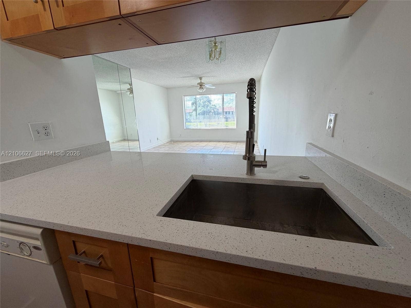 Kitchen featuring a stone-composite countertop, undermount stainless steel basin, and industrial-style faucet with a high-arch pull-down sprayer, complemented by natural wood-finish cabinetry