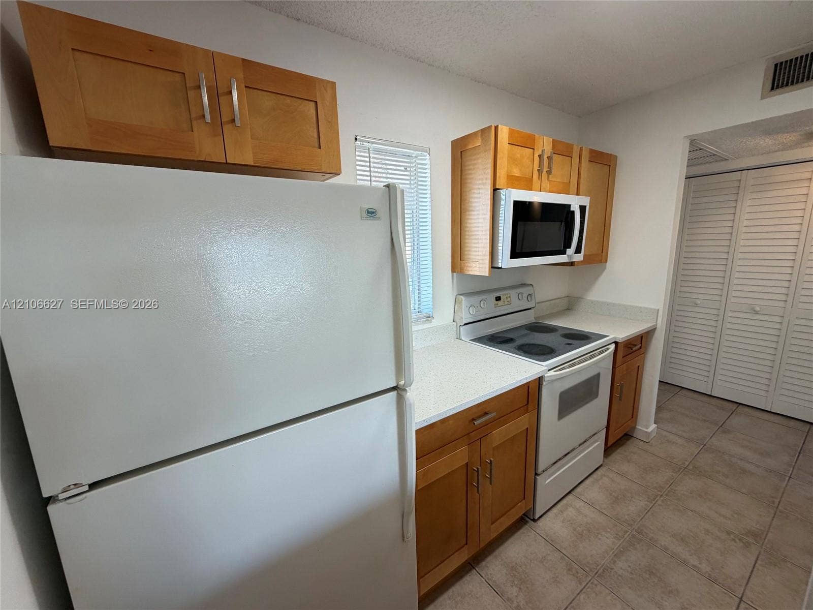 Kitchen featuring shaker-style wood cabinetry, stone-finish countertops, tile flooring, and integrated white appliances including a microwave and range