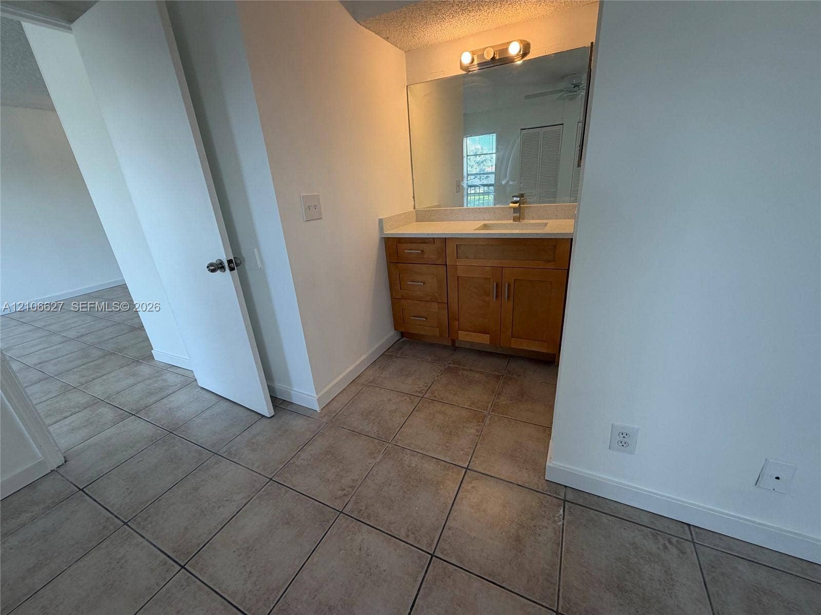9954 Twin Lakes Drive, #7-O, Coral Springs, Coral Springs, FL 33071 Bathroom vanity featuring a wood-finish cabinet, solid surface countertop with an integrated sink, polished metal faucet, and wall-mounted light fixture above a large mirror, finished with ceramic tile flooring