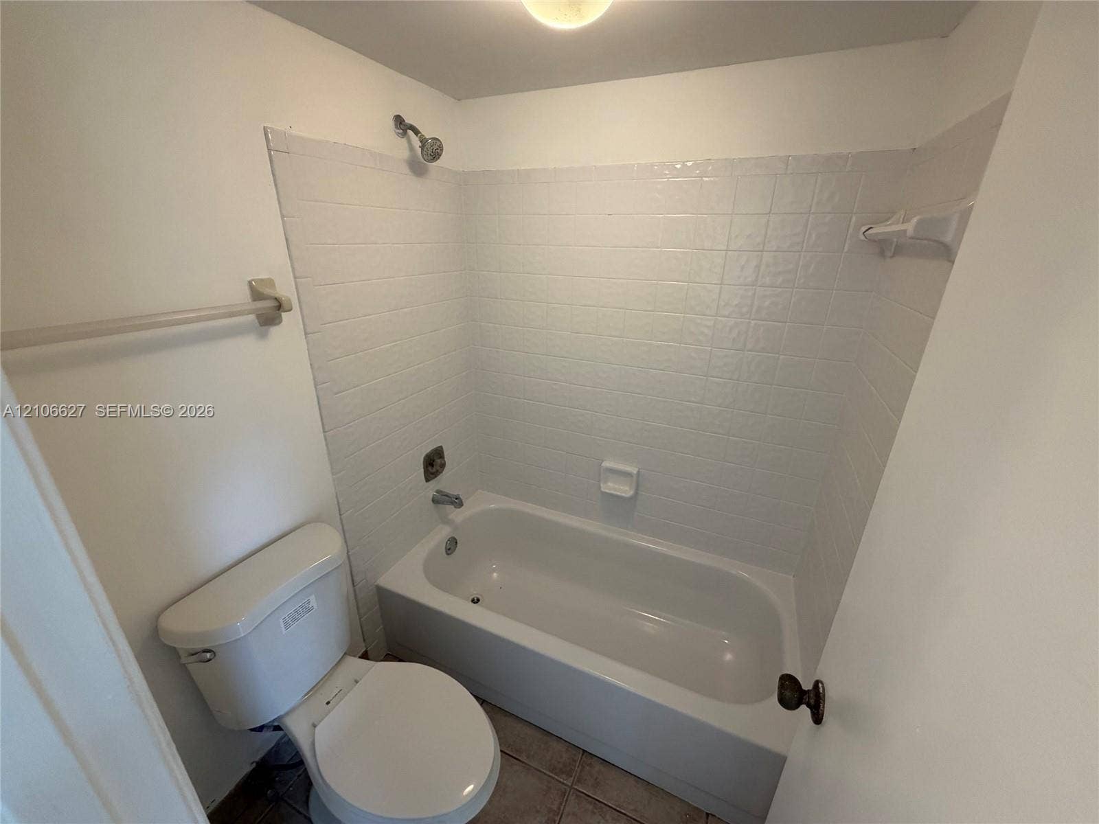 Bathtub and shower combination with white square tile surround, ceramic tile flooring, chrome hardware, and white toilet