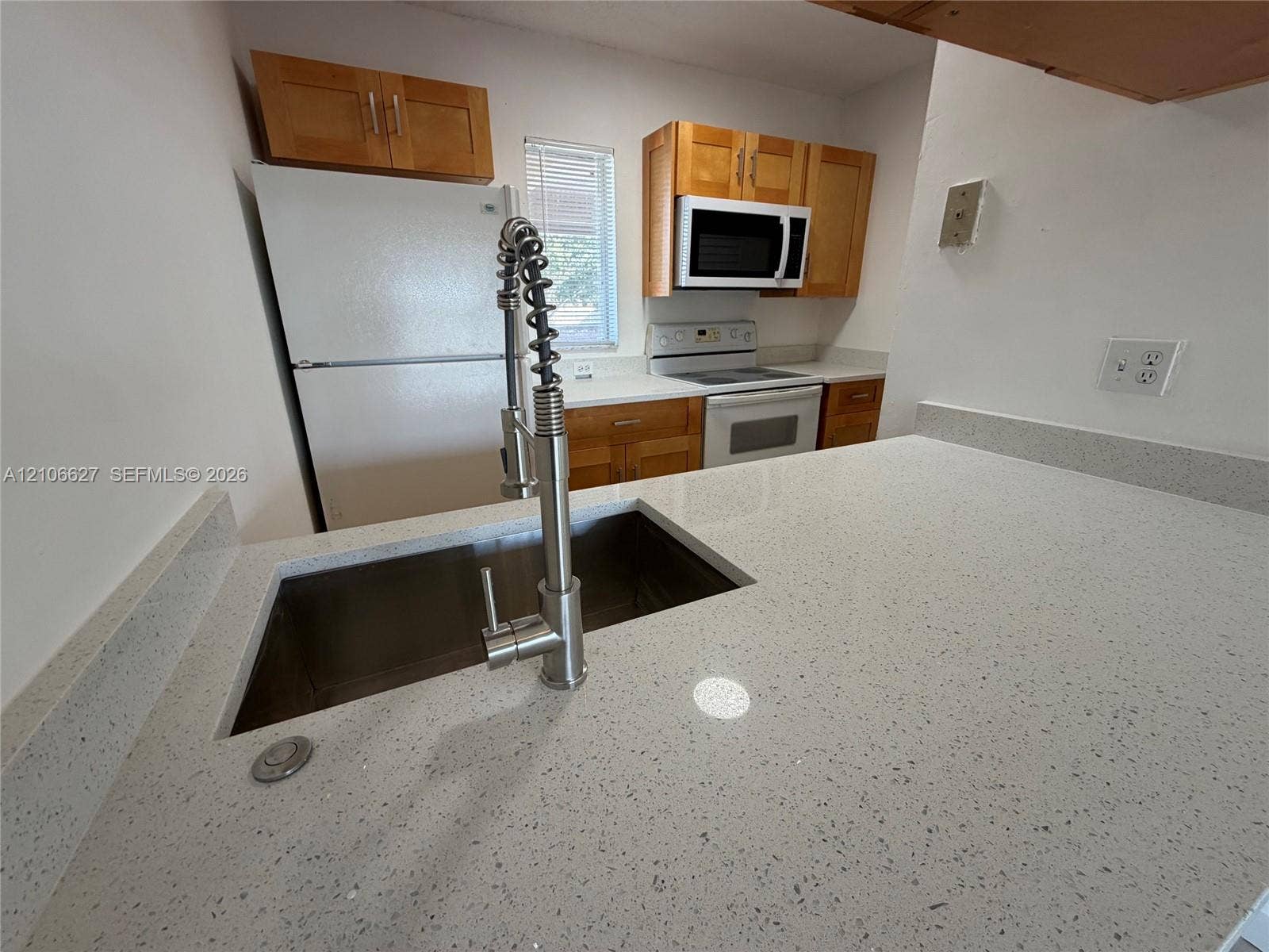 Kitchen featuring light-toned cabinetry, solid surface countertops, a stainless steel undermount sink, a gooseneck faucet, and built-in appliances