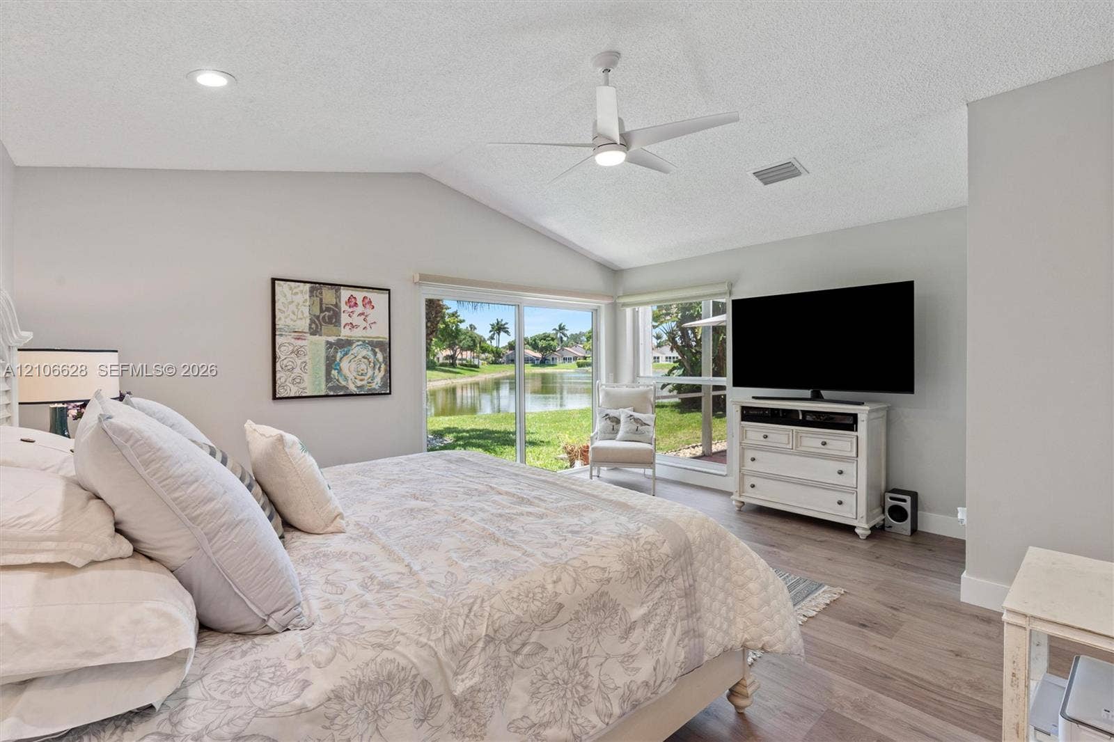 7259 Via Palomar, Boca Raton, FL 33433 Vaulted ceiling with integrated lighting, wood-finish flooring, and expansive sliding glass doors opening to a water feature