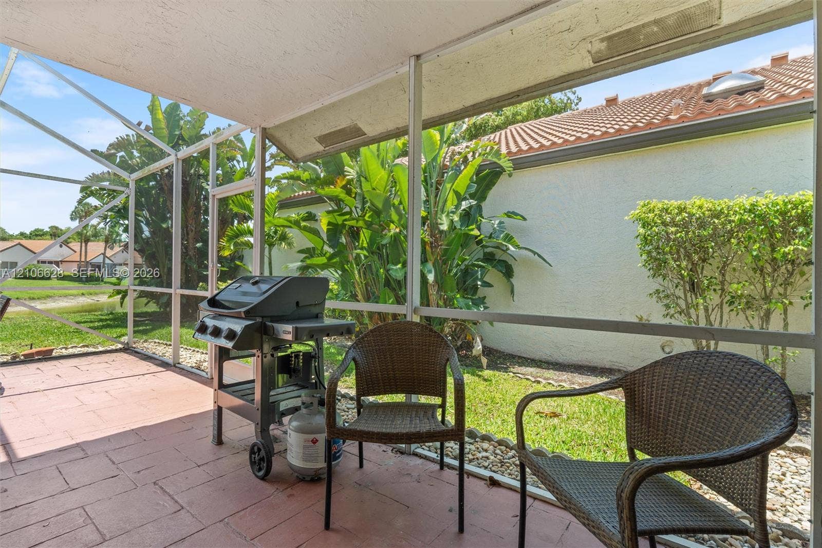 7259 Via Palomar, Boca Raton, FL 33433 Screen-enclosed patio featuring masonry tile flooring, metal frame construction, and direct access to an outdoor area with mature vegetation