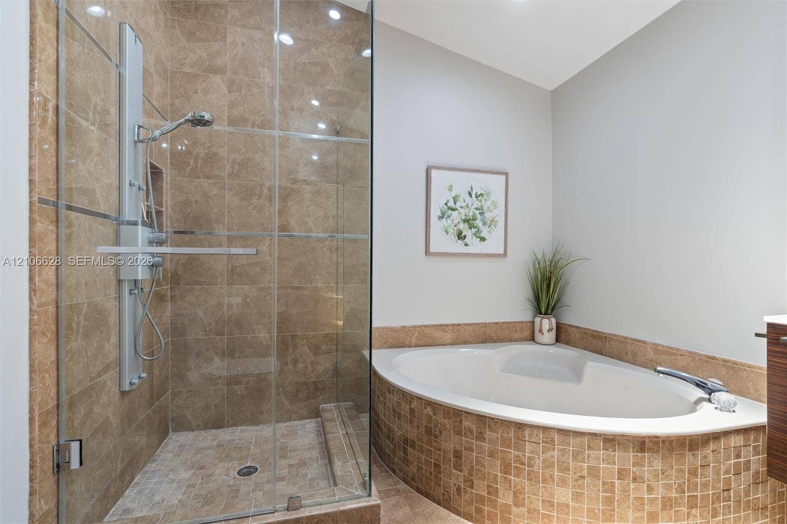 7259 Via Palomar, Boca Raton, FL 33433 Walk-in shower with stone tile surround, frameless glass enclosure, and wall-mounted shower panel, paired with a corner soaking tub featuring a stone tile skirt and matching deck