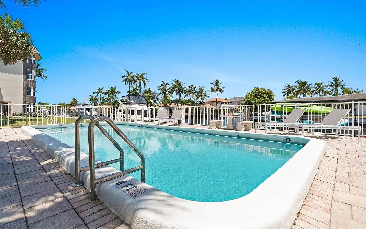 Swimming pool featuring a concrete deck, metal handrails, and a white perimeter fence