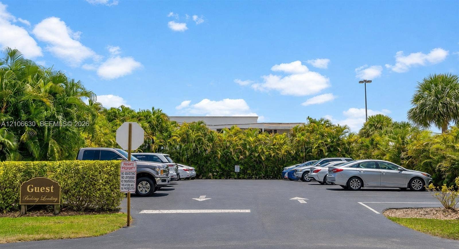 Dedicated guest parking area featuring paved asphalt surfaces, marked parking stalls, directional signage, and mature perimeter landscaping