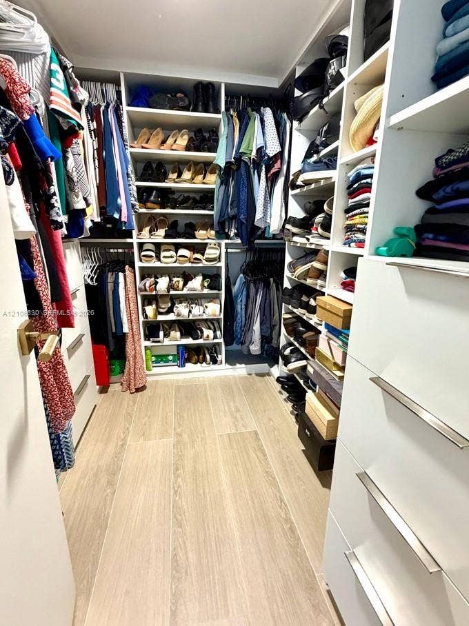 Walk-in closet featuring extensive white built-in shelving, hanging rods, integrated drawer storage with metal pulls, and wood-finish flooring