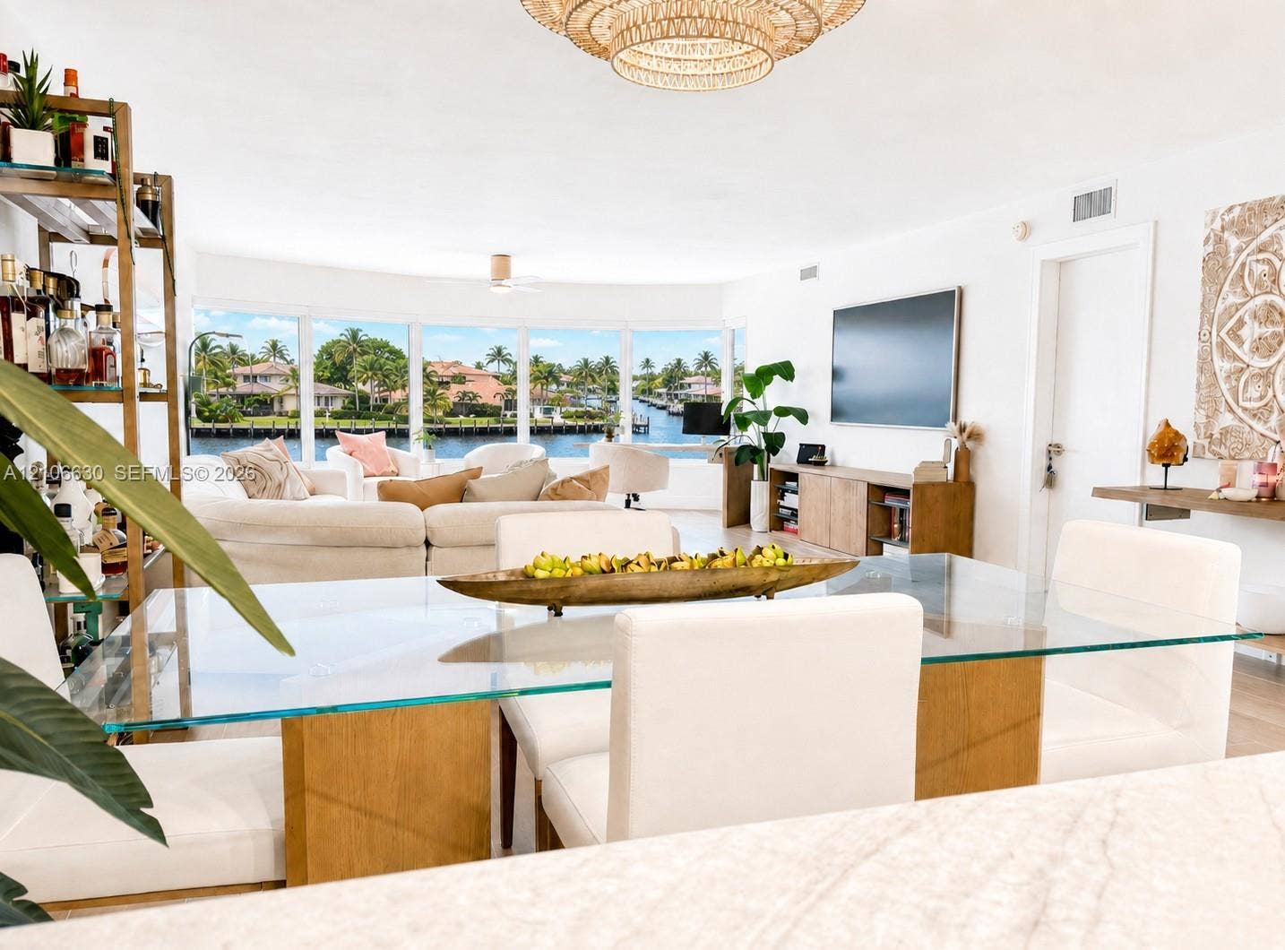 Open-concept living space featuring floor-to-ceiling windows, waterfront scenery, and an intricate woven pendant light fixture