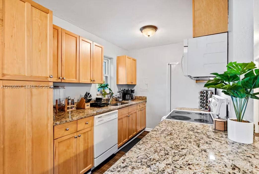 Kitchen featuring natural wood cabinetry, stone countertops, integrated microwave, built-in dishwasher, and a glass-top electric range