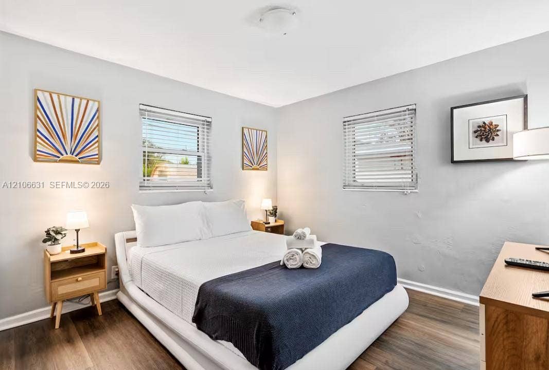 Room with wood-finish flooring, neutral wall paint, and two windows featuring horizontal blinds