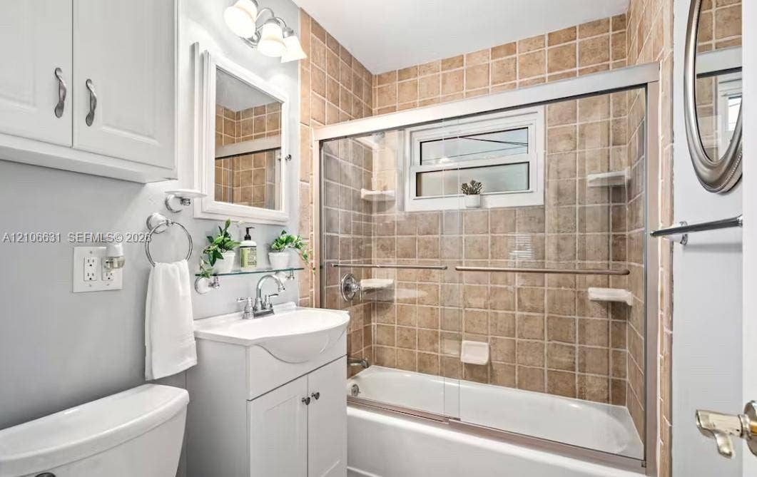 Bathroom featuring a white vanity cabinet with a integrated basin, sliding glass shower doors, tile-surround tub, framed wall mirror, and vanity lighting