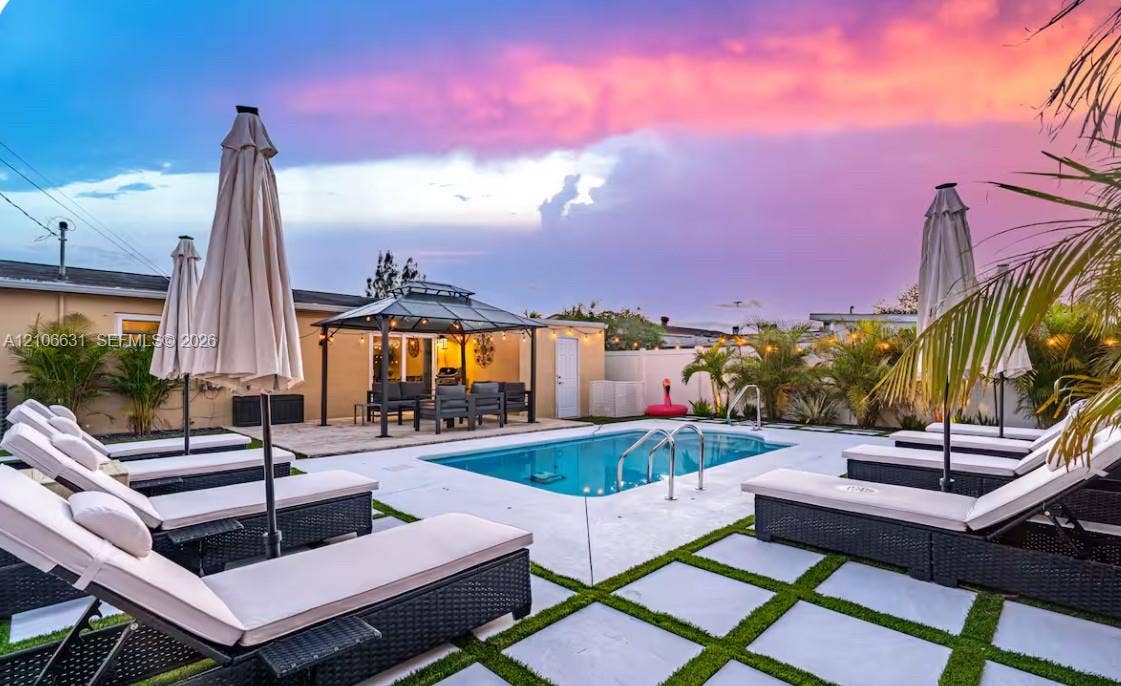 In-ground swimming pool with metal ladder, stone-paver pool deck, grass-grid inlay, and metal-frame gazebo