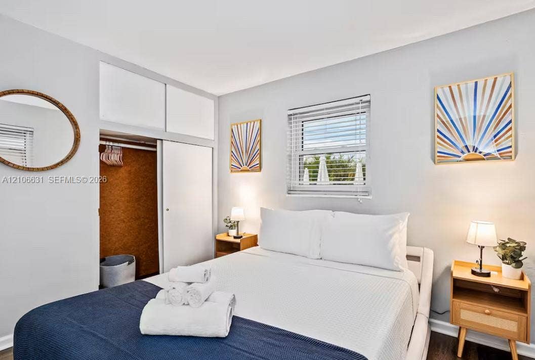 Bedroom featuring neutral-toned walls, wood-finish flooring, a double-hung window with blinds, and built-in closet cabinetry with sliding doors