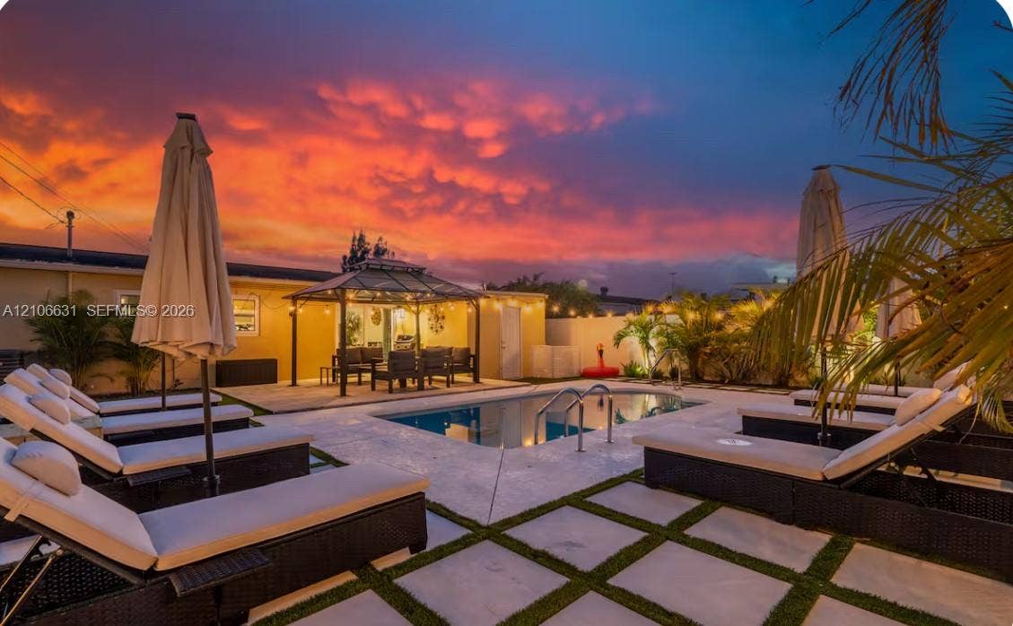 In-ground swimming pool featuring a concrete deck with turf inlay, metal-framed gazebo, and perimeter privacy wall