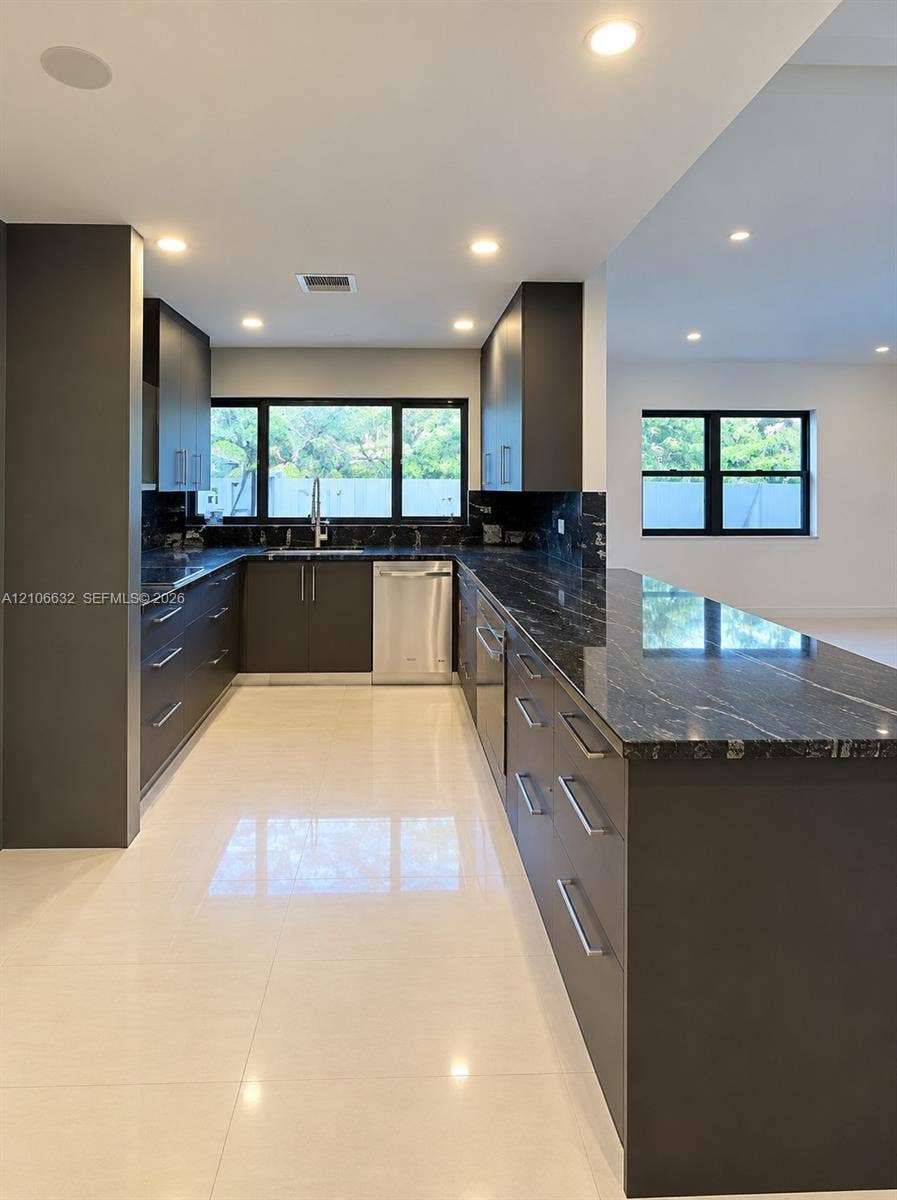 Kitchen featuring dark cabinetry, expansive stone countertops, stainless steel appliances, recessed ceiling lighting, and large-format tile flooring