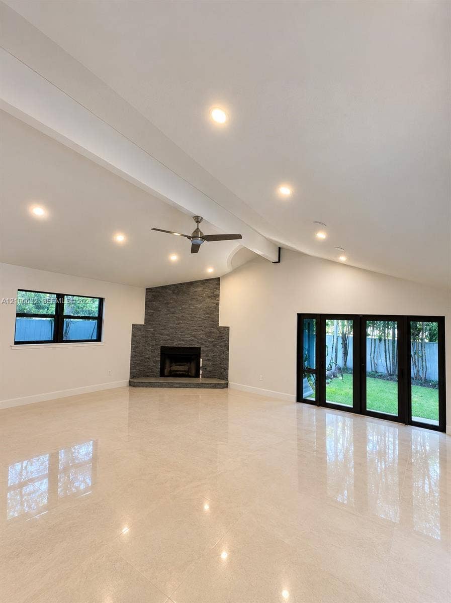 Vaulted ceiling with recessed lighting, stone-surround fireplace, polished tile flooring, ceiling fan, and black-framed multi-panel sliding glass doors