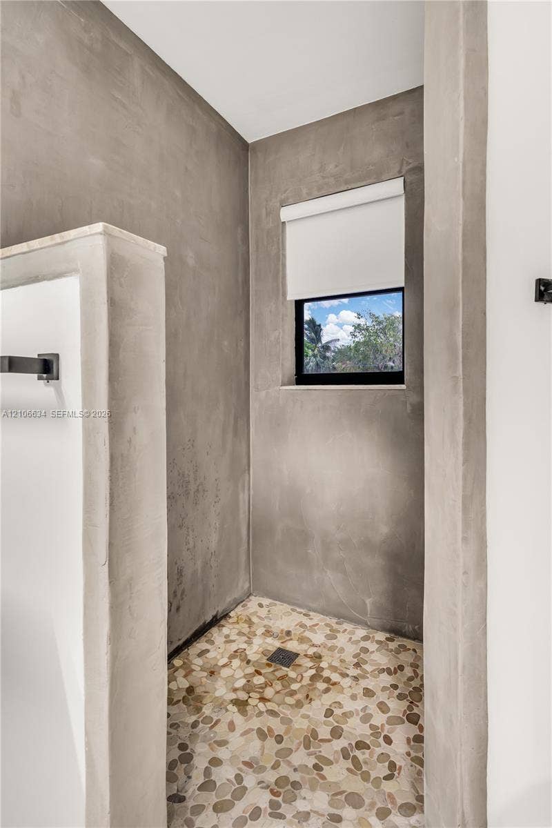 Shower enclosure featuring cement-finish walls, a river rock stone floor, recessed window, and matte black hardware