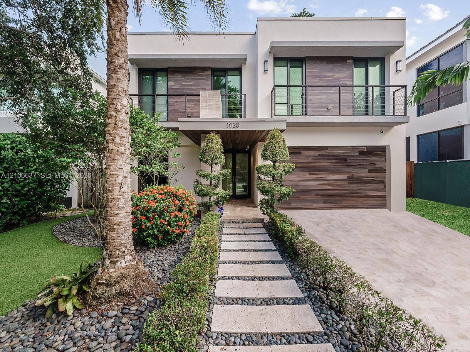 Contemporary two-story exterior featuring smooth stucco facade, horizontal wood-finish cladding, second-story balcony with metal railing, and paver walkway set in stone aggregate