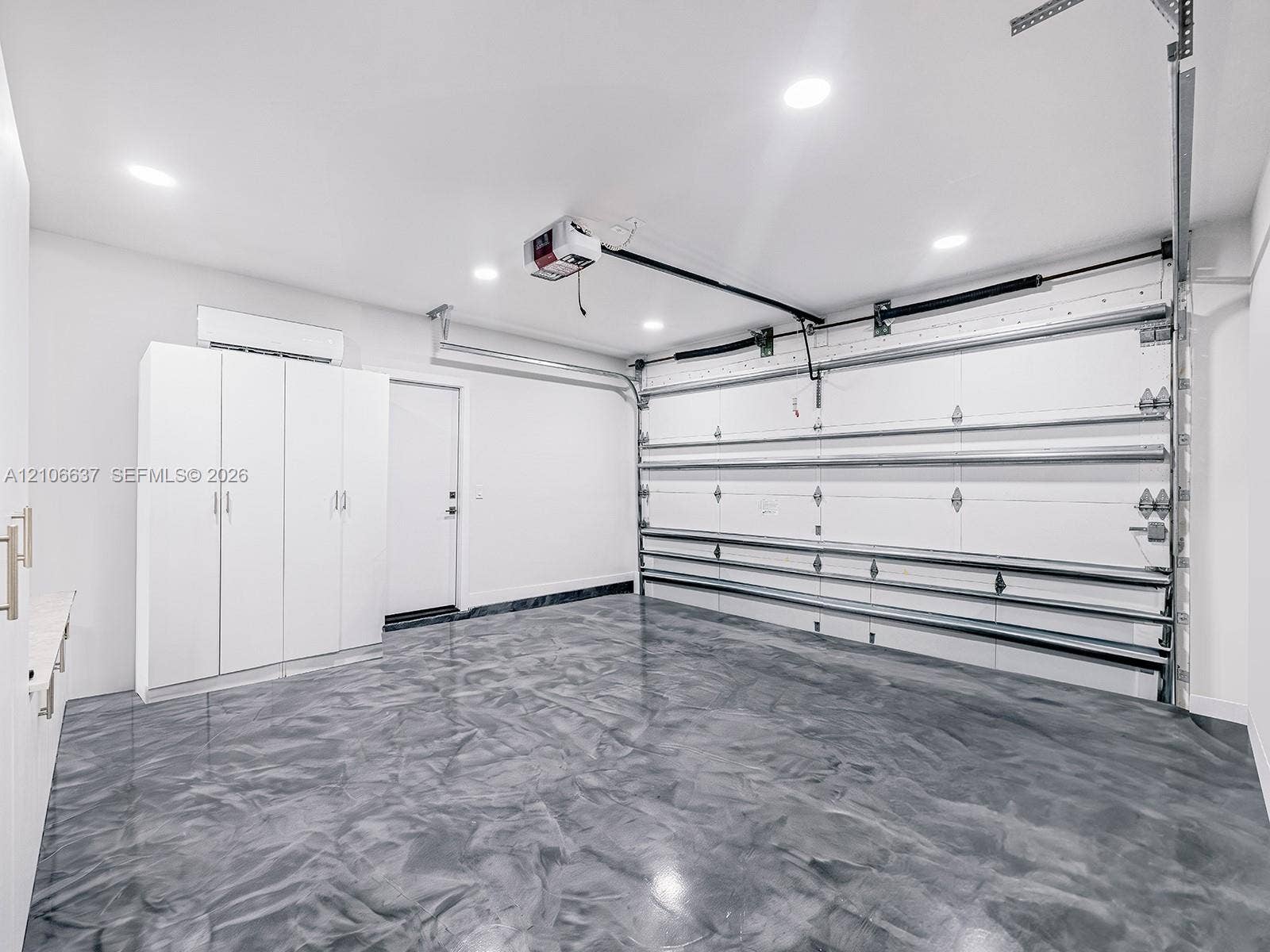 Garage featuring high-gloss epoxy flooring, built-in white cabinetry, recessed LED lighting, and a climate control unit