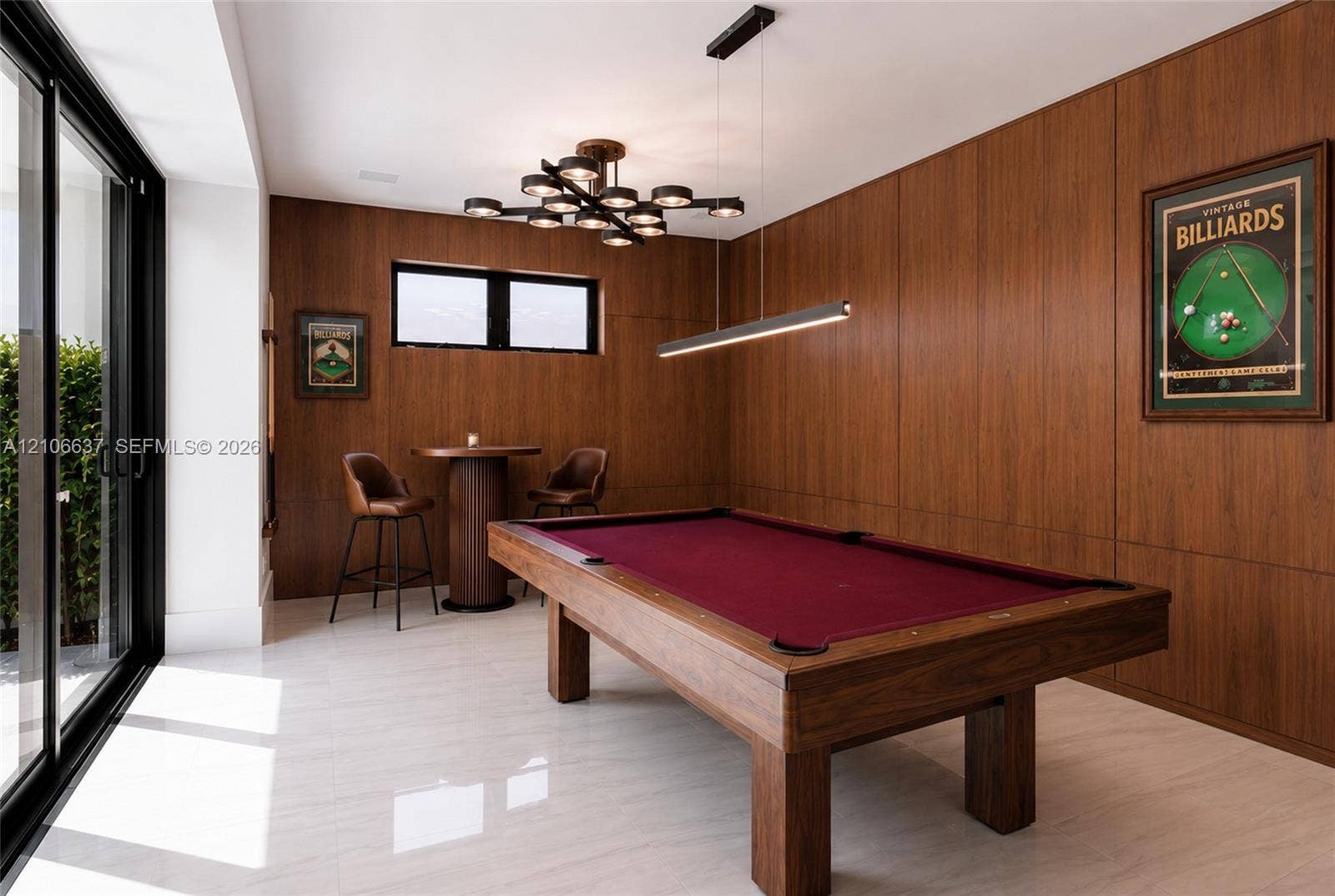 Wood-paneled walls, large-format tile flooring, multi-light modern chandelier, horizontal linear pendant light, and black-framed sliding glass doors
