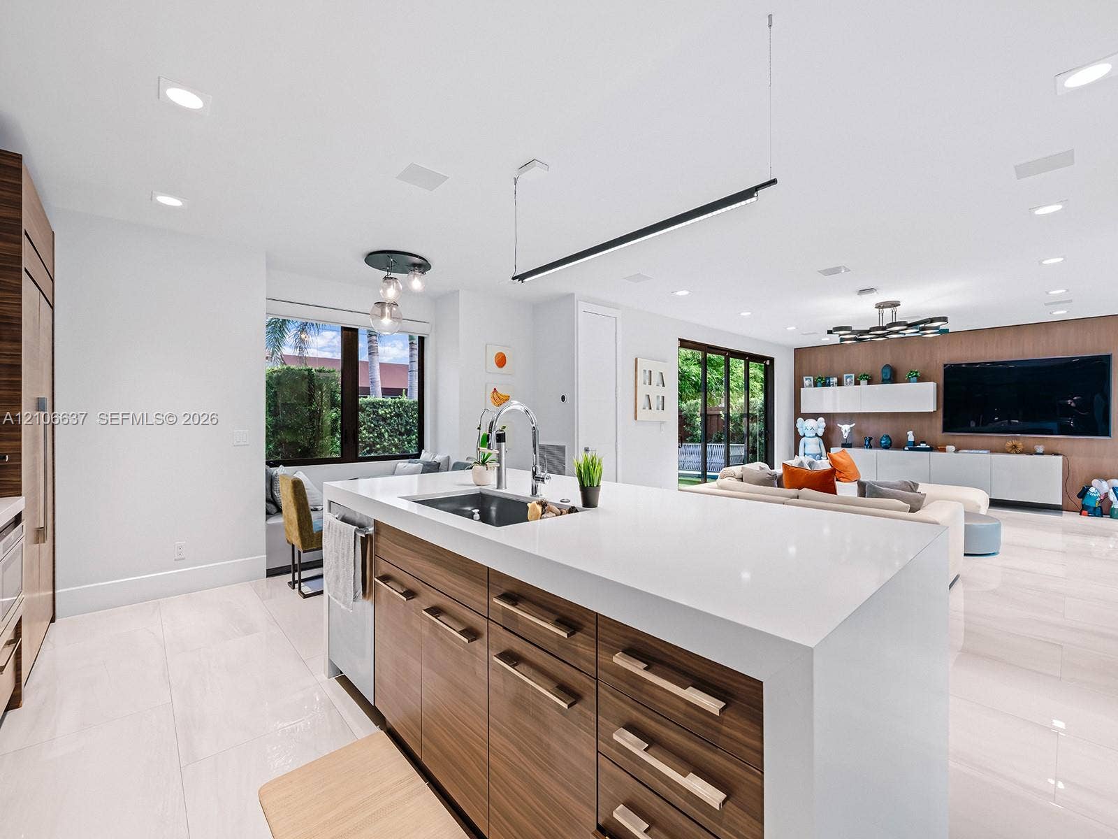 Kitchen island featuring a waterfall quartz countertop, undermount sink, integrated gooseneck faucet, and wood-finish cabinetry with metallic hardware