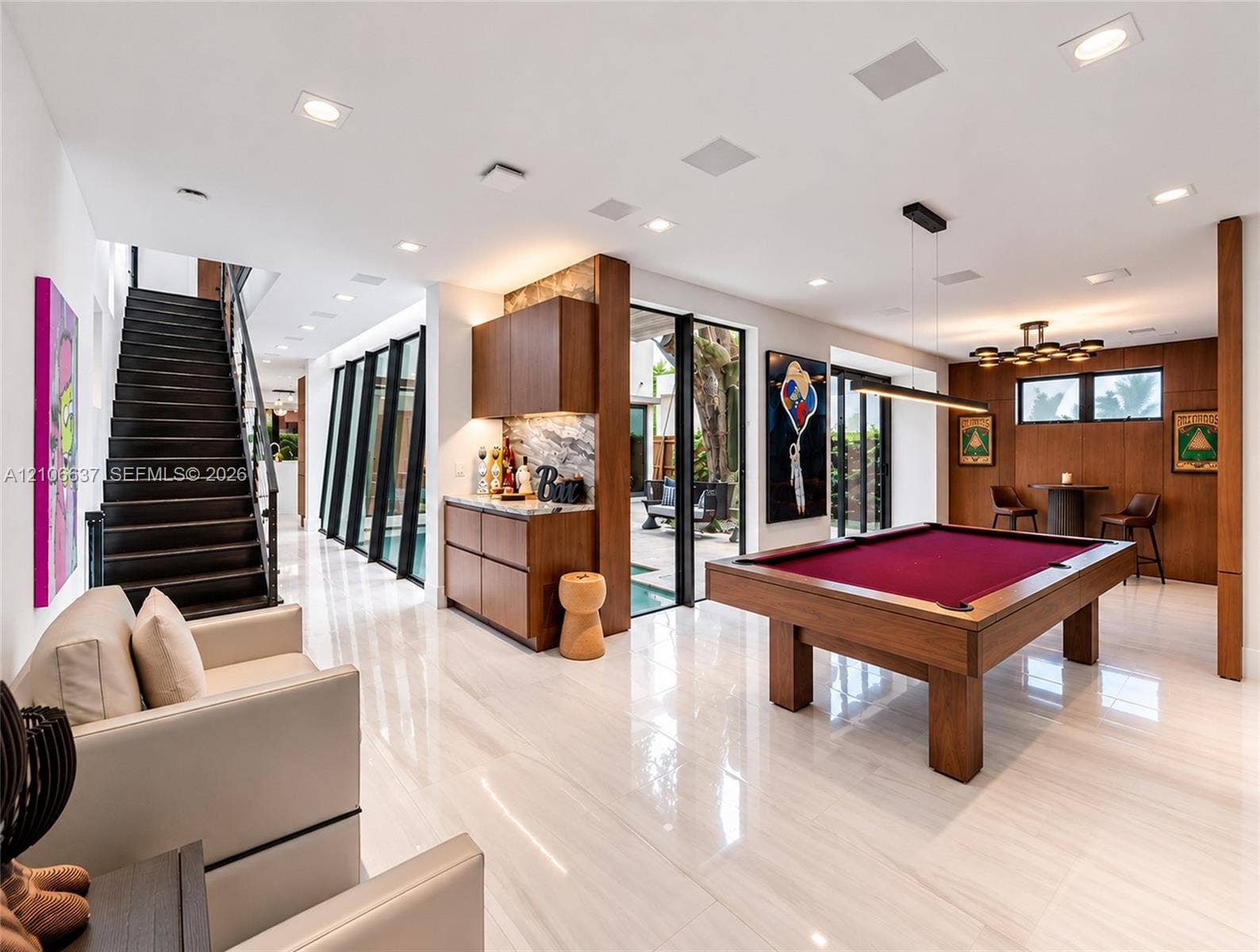Polished stone flooring, wood-panelled accent walls, integrated bar cabinetry with stone backsplash, staircase with open risers, and floor-to-ceiling glass paneling