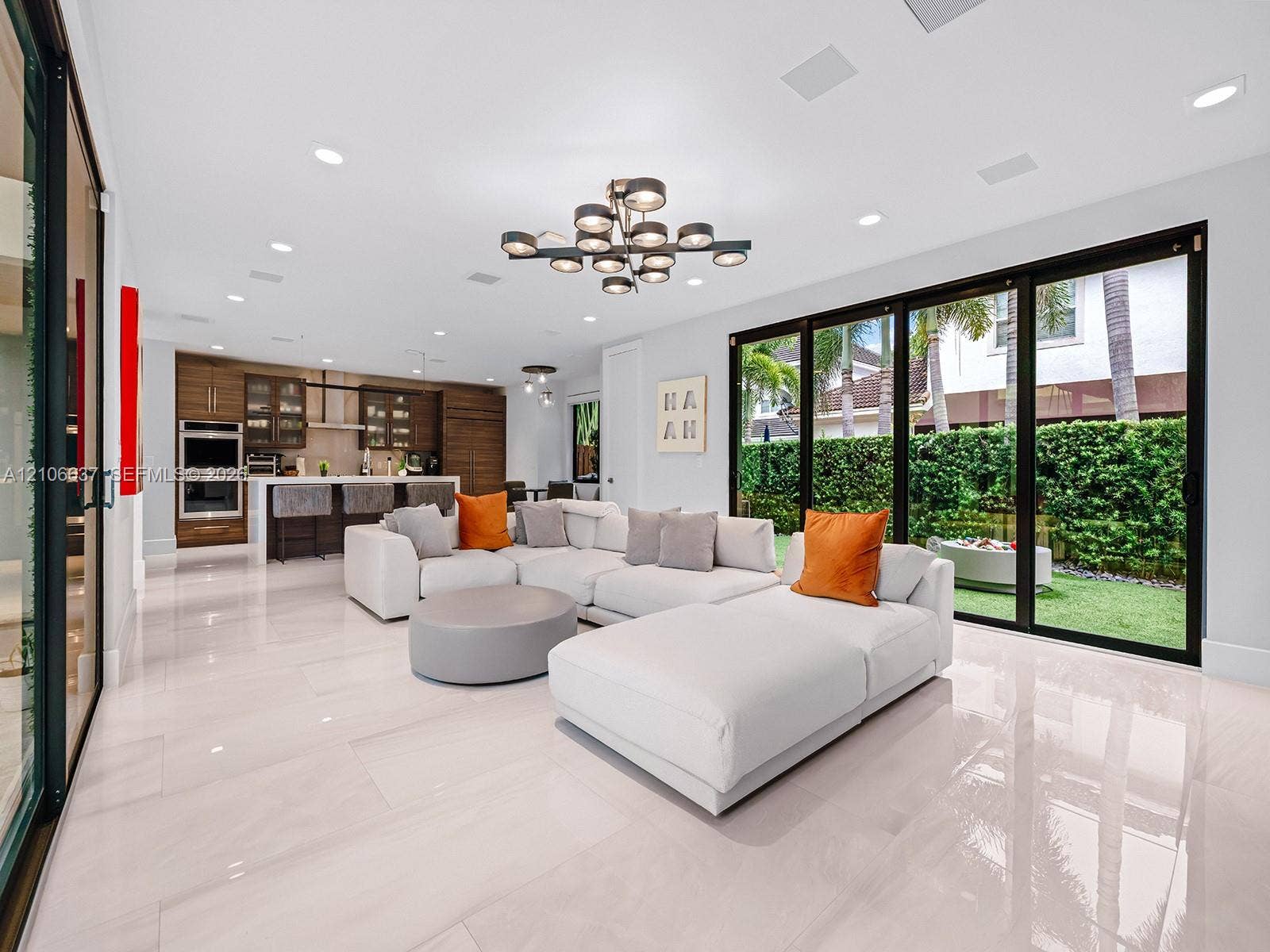 Open-concept living space featuring large-format tile flooring, multi-panel sliding glass doors, built-in cabinetry, recessed lighting, and a modern tiered chandelier