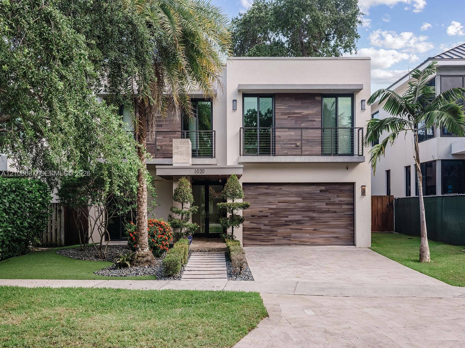 Contemporary two-story exterior featuring wood-finish siding, a private balcony with horizontal metal railings, a modern garage door, and a stone-paver walkway