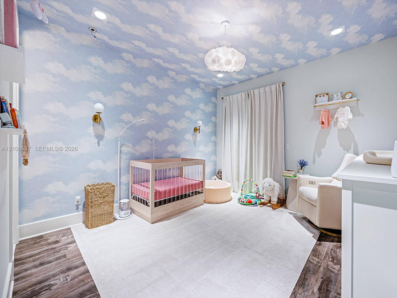 Room featuring cloud-patterned wallpaper extending to the ceiling, wood-finish flooring, dual wall-mounted brass light fixtures, recessed ceiling lighting, and a textured sphere pendant light