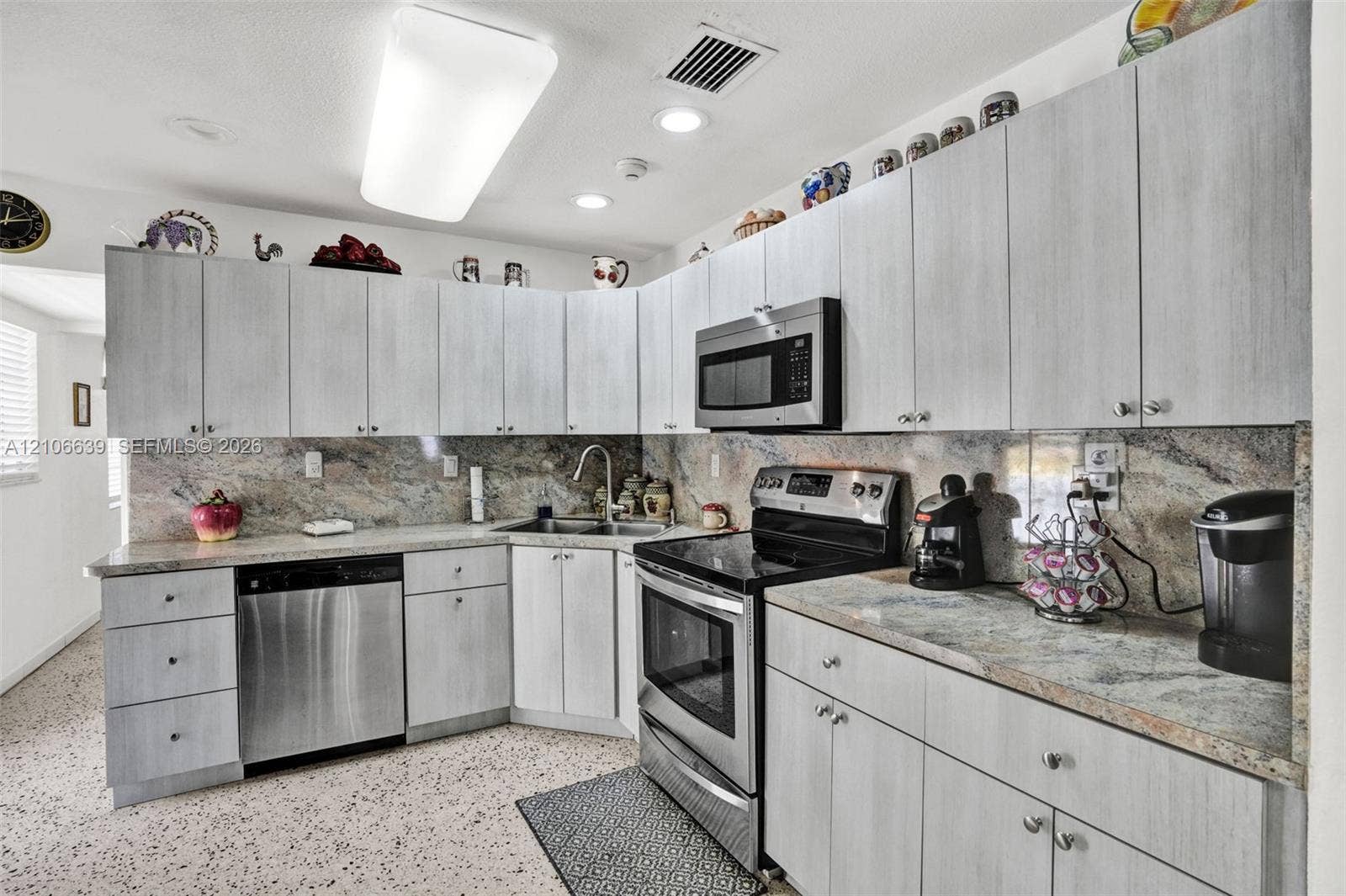 Kitchen featuring light-toned cabinetry, natural stone countertops with matching backsplash, stainless steel appliances, and integrated recessed lighting
