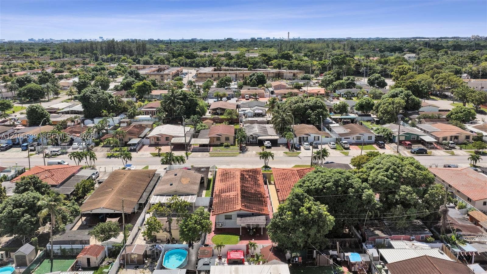 Aerial perspective featuring a residential lot with a paved driveway, built-in swimming pool, mature canopy trees, and tile roof construction