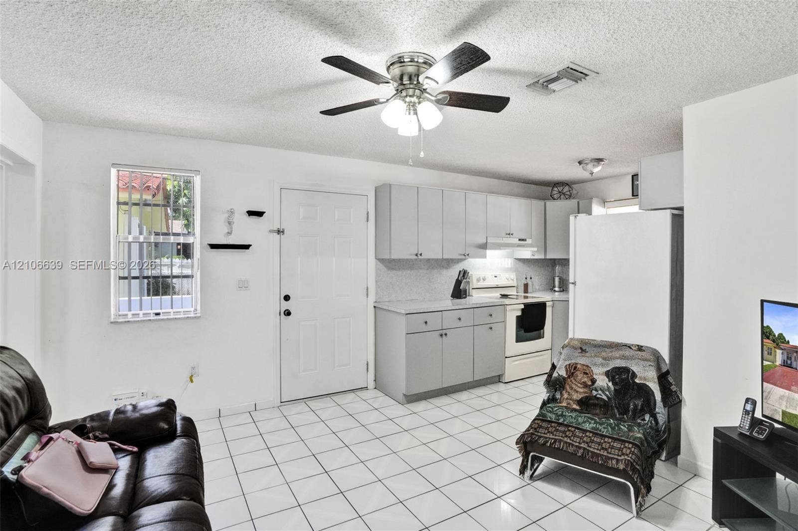 Kitchen featuring light gray cabinetry, solid surface countertops, tile flooring, a ceiling fan with integrated lighting, and a window with security bars
